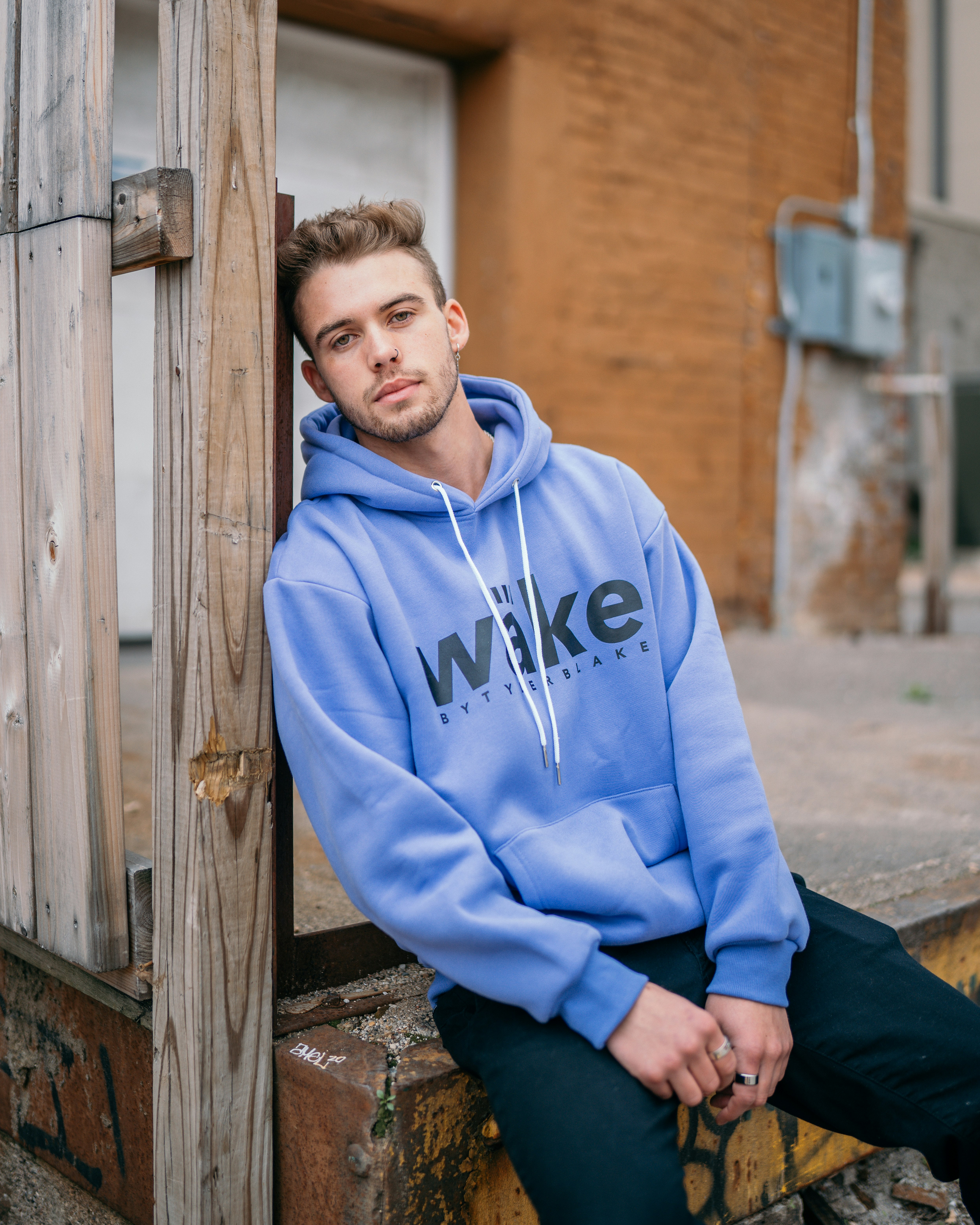 boy in blue and white pullover hoodie standing beside brown wooden wall during daytime